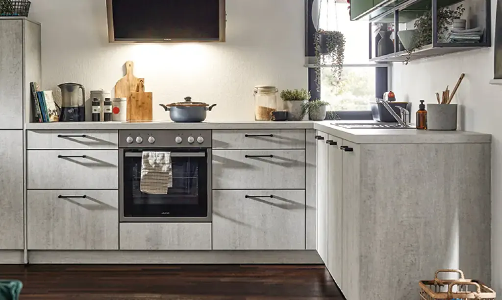Helle Küche in Betonoptik mit Herdzeile links und Spülbereich rechts, dunkle Griffe und Holzdetails, moderne Küchenmöbel